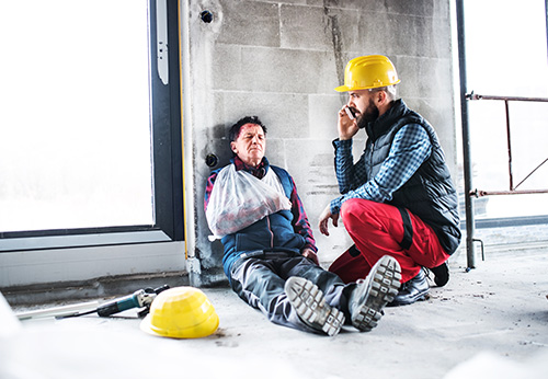 Injured construction worker with arm cast filling out a report at desk with hard hat.